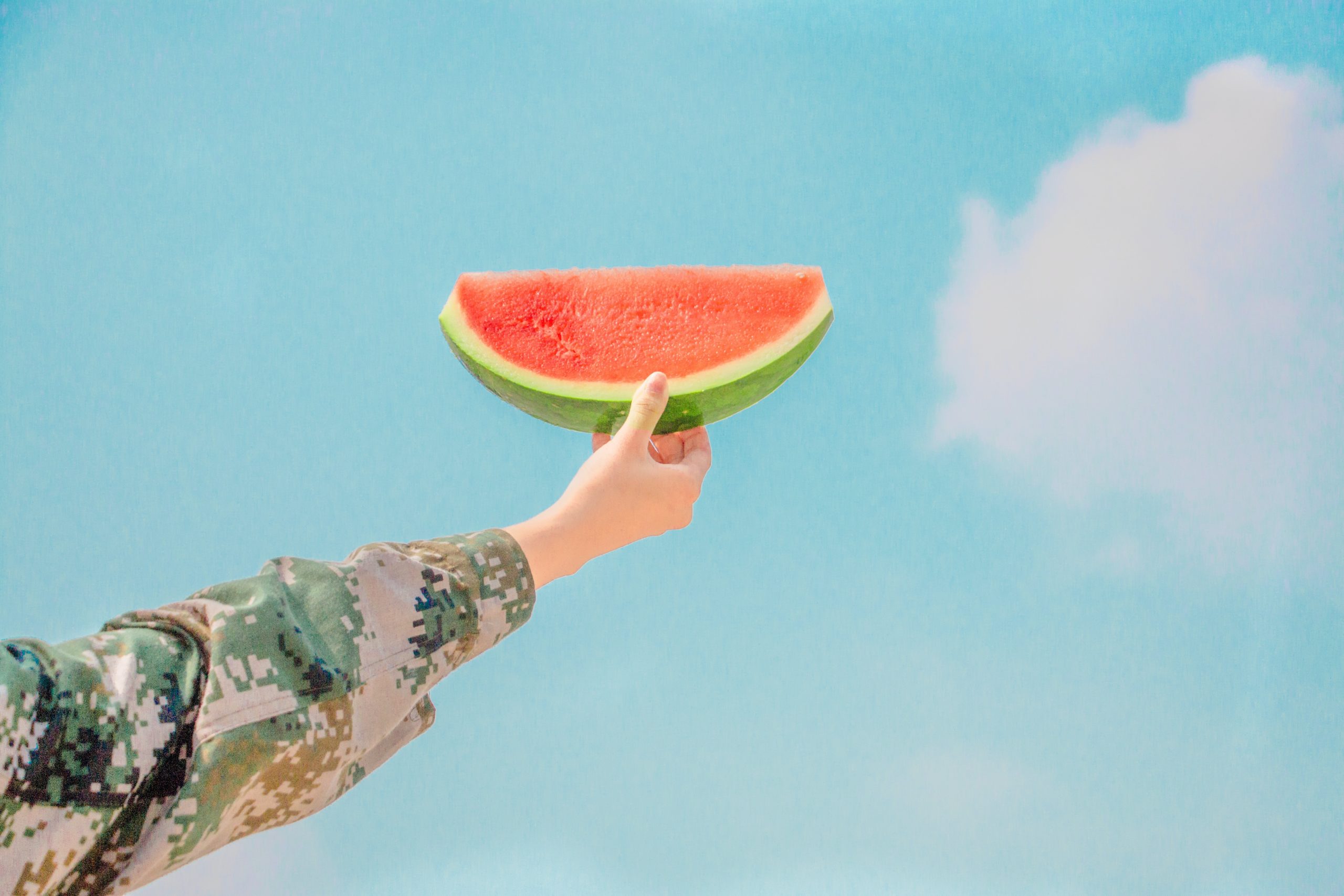 woman holding slice of watermelon up with blue sky in background